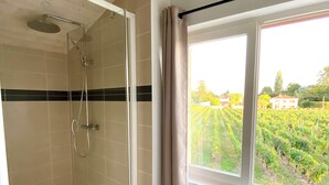 A bathroom with a glass shower, a window with a view of a vineyard, and a wooden ceiling. - Chambre d’hôtes de Austerlitz (Libourne)