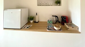 A compact kitchen with a white refrigerator, a small sink, a coffee maker, a kettle, and a basket of bread. - Chambre d’hôtes de Austerlitz (Libourne)