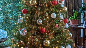 A Christmas tree decorated with ornaments and lights, placed in a room with a window and curtains.