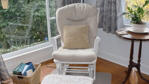 A cozy room with a white rocking chair, a small table with a potted plant, and a wicker basket on the floor.