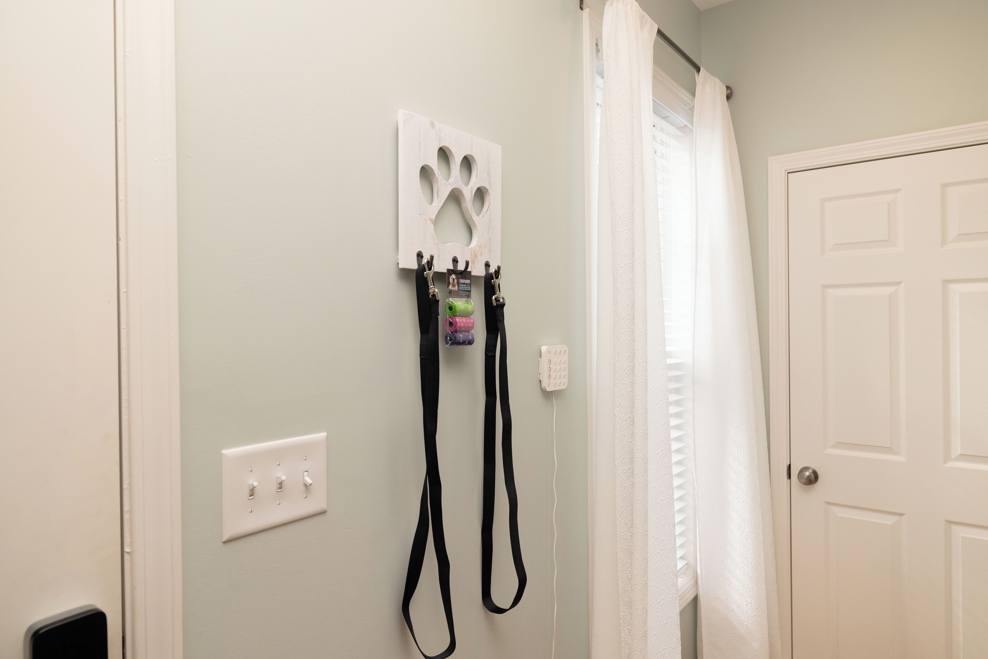 Une salle de bain décorée avec une empreinte de patte de chien fixée au mur, un porte-serviettes avec une serviette violette et verte, et une porte blanche.