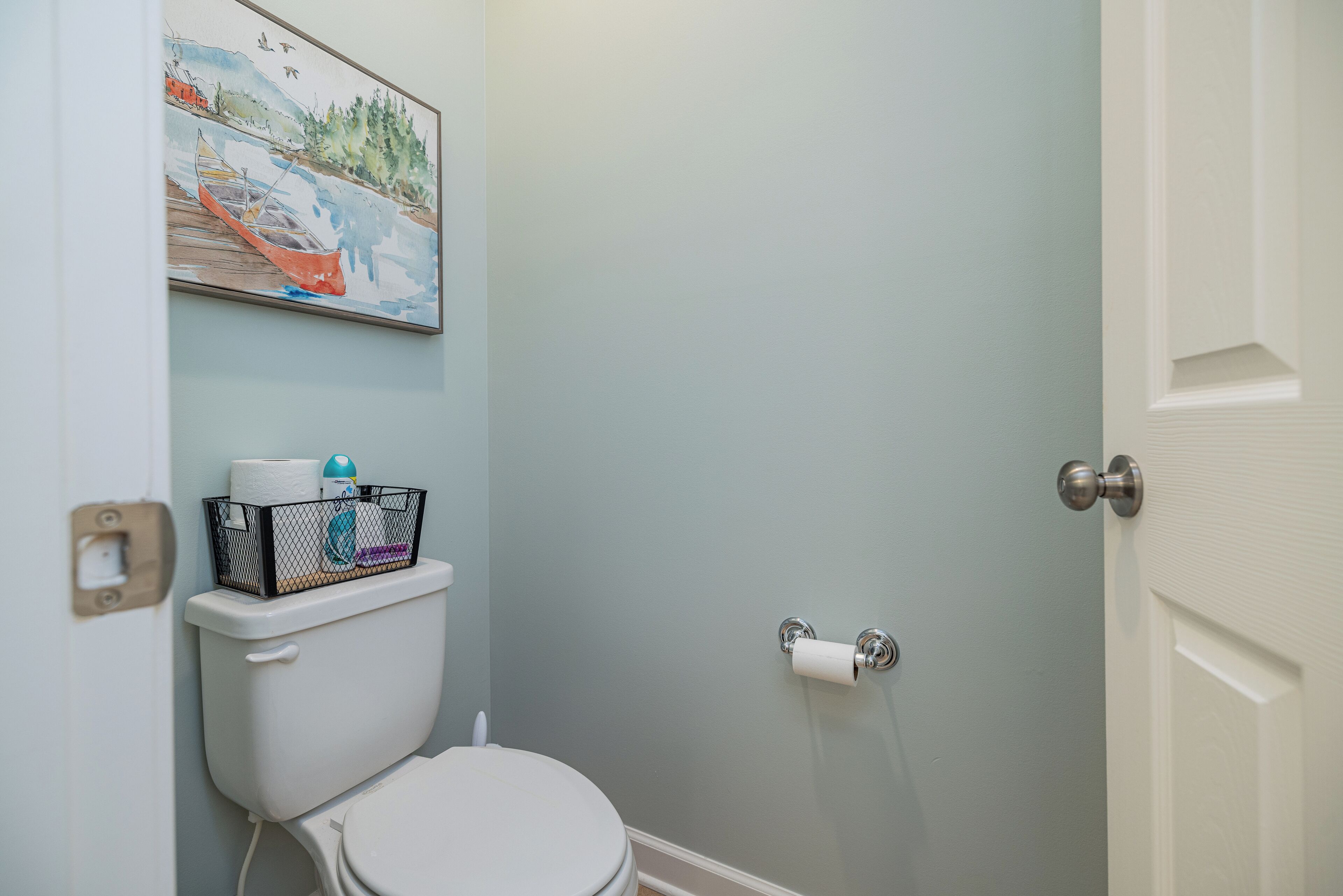 Une salle de bain avec des toilettes, un tableau représentant un bateau sur l’eau et une porte.