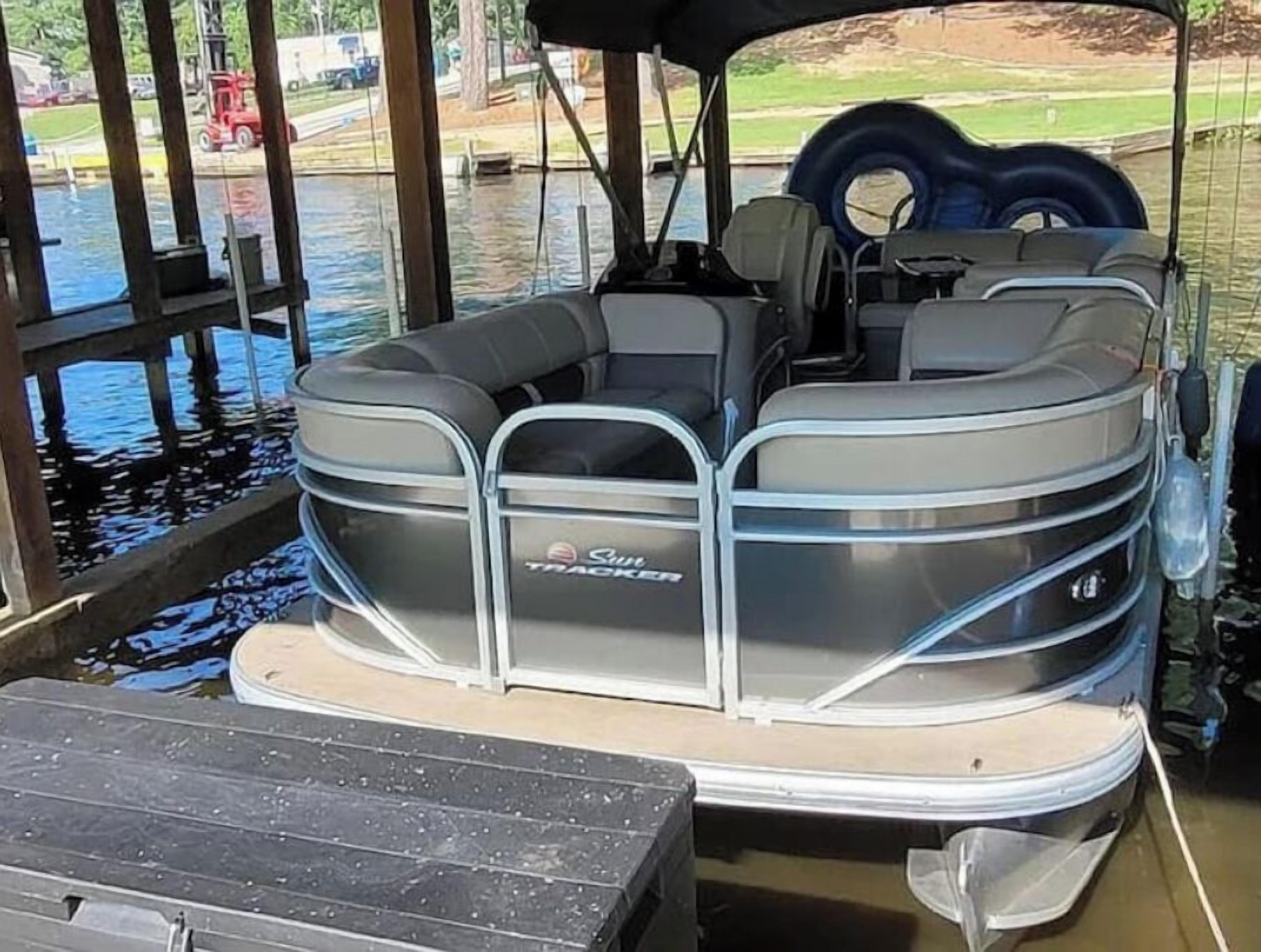 A pontoon boat with a covered seating area, a storage compartment, and a wakeboard.