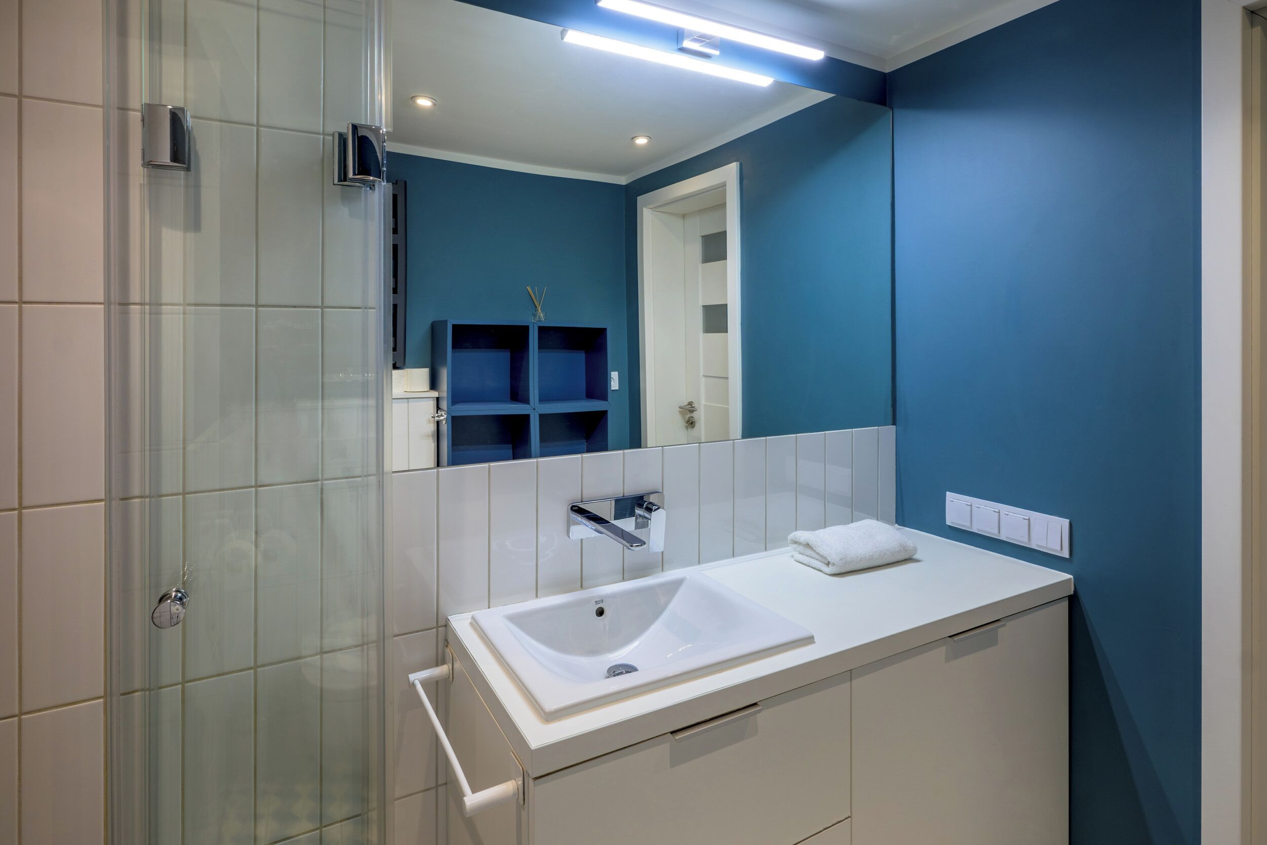 A modern bathroom with a large mirror, white sink, and blue walls.