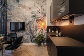 A modern kitchen with a large floral mural, a flat-screen TV, and a dining area with black chairs and a glass table. - RentPlanet - Apartament Kotlarska (Wroclaw)