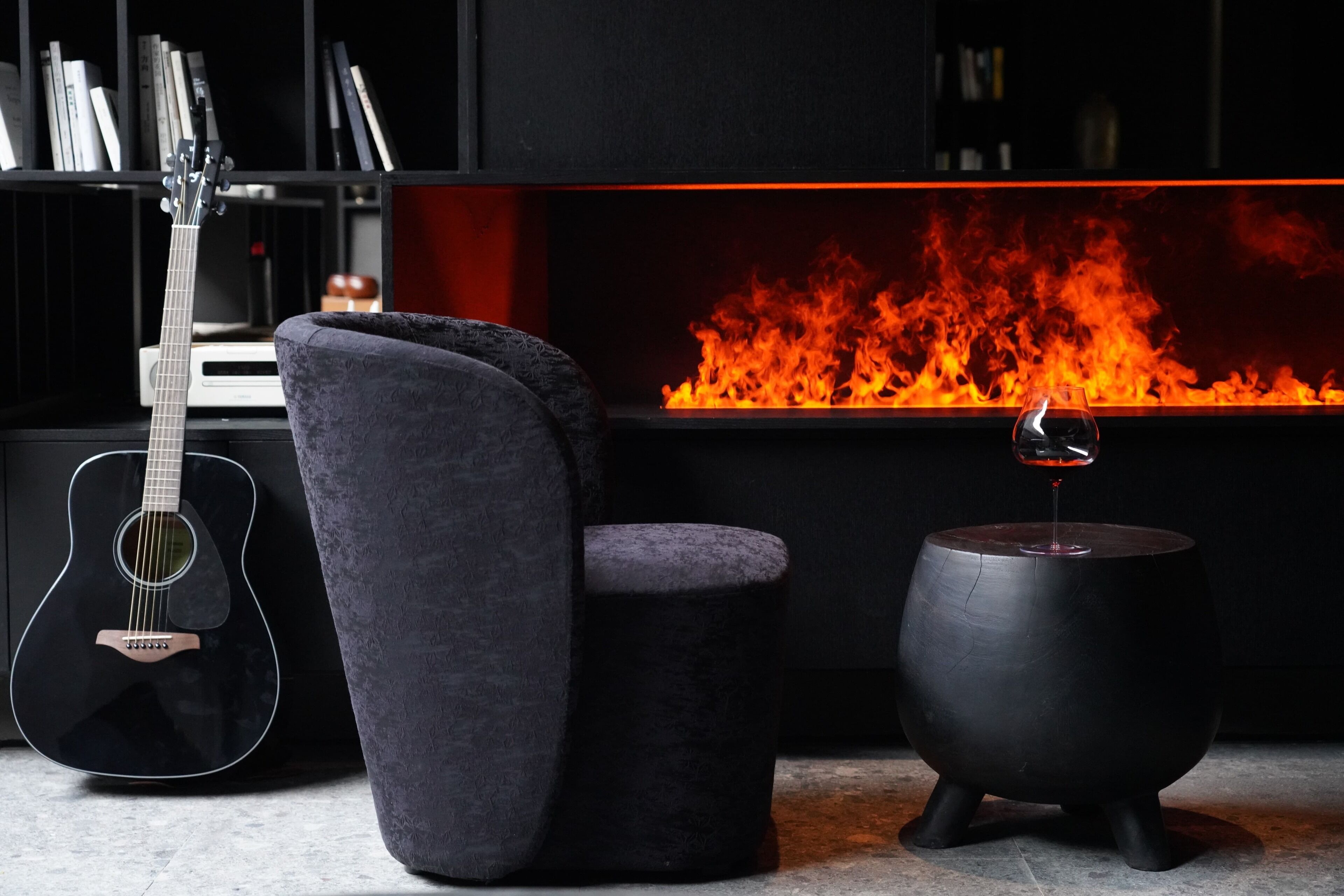 Una sala de estar moderna con chimenea, una guitarra negra, un sillón mullido y una mesa redonda negra.