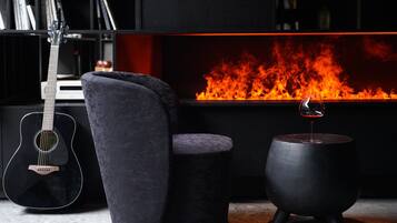 Una sala de estar moderna con chimenea, una guitarra negra, un sillón mullido y una mesa redonda negra.