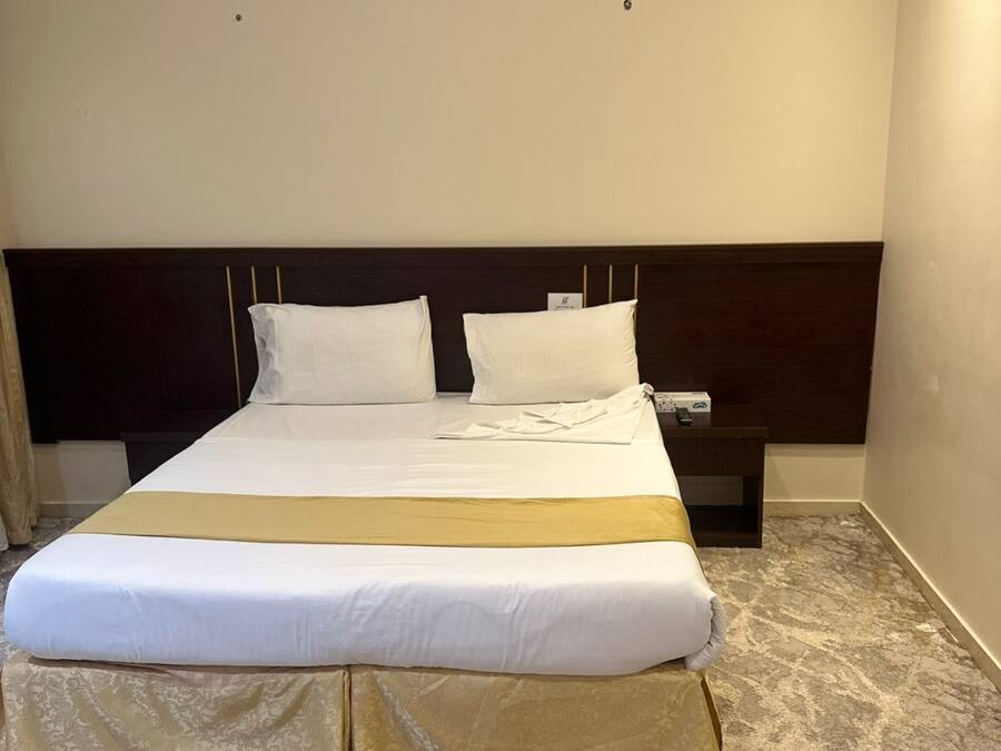 A neatly made bed with a headboard, a bedside table with a lamp, and a patterned carpet.