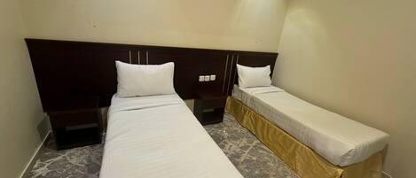 Una camera d'albergo con due letti singoli, una testata del letto scura, un pavimento effetto marmo e un lampadario a parete.