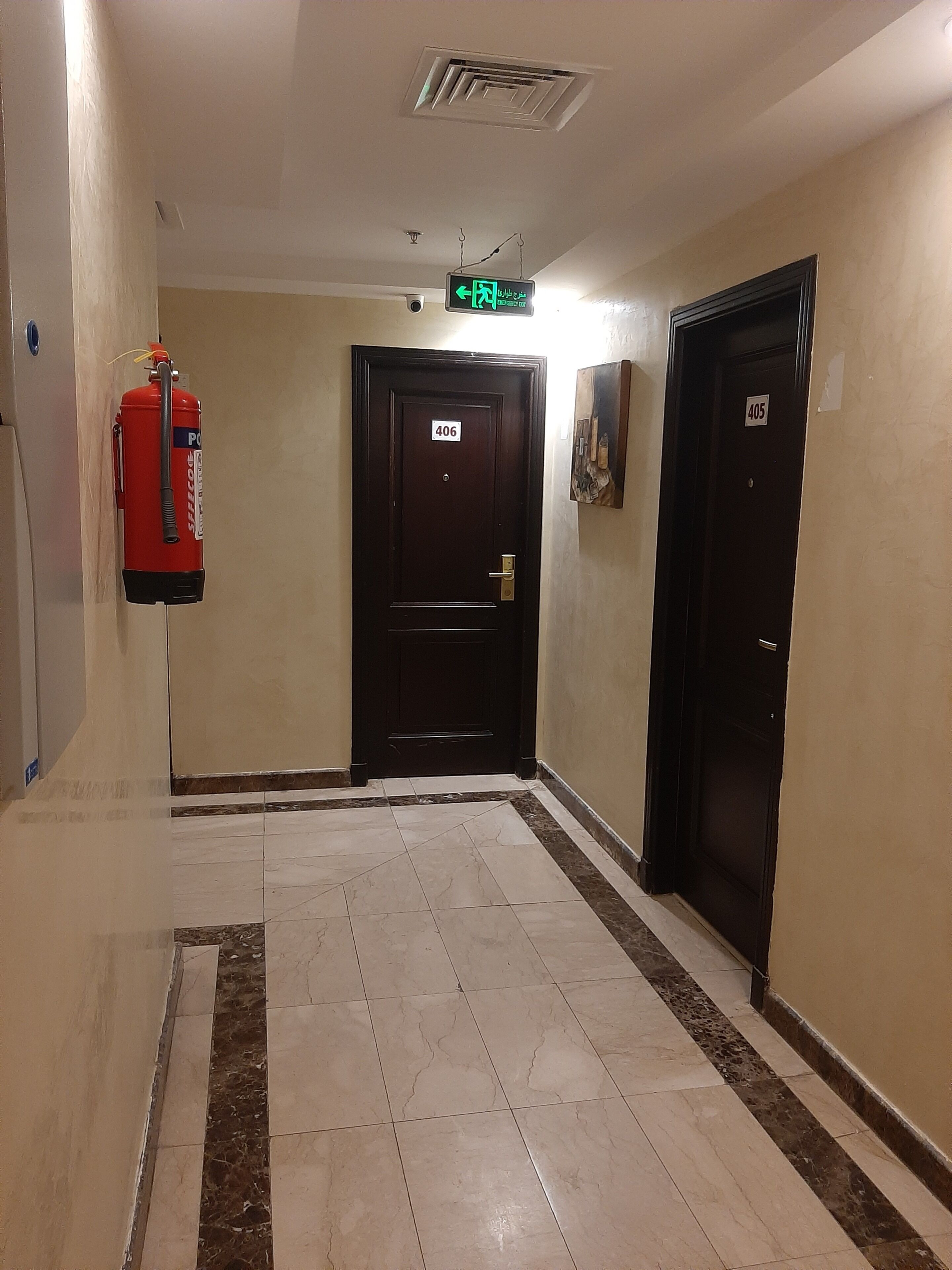 A corridor with a fire extinguisher, two doors labeled 406 and 405, and a green exit sign.