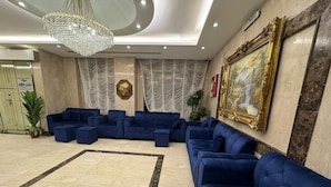 A spacious lobby with a large blue sofa set, a chandelier, and a framed painting on the wall. - Taj Aldahabia Hotel - Makkah - Al Rawda فندق تاج الذهبية - مكة - الروضة (Makkah)