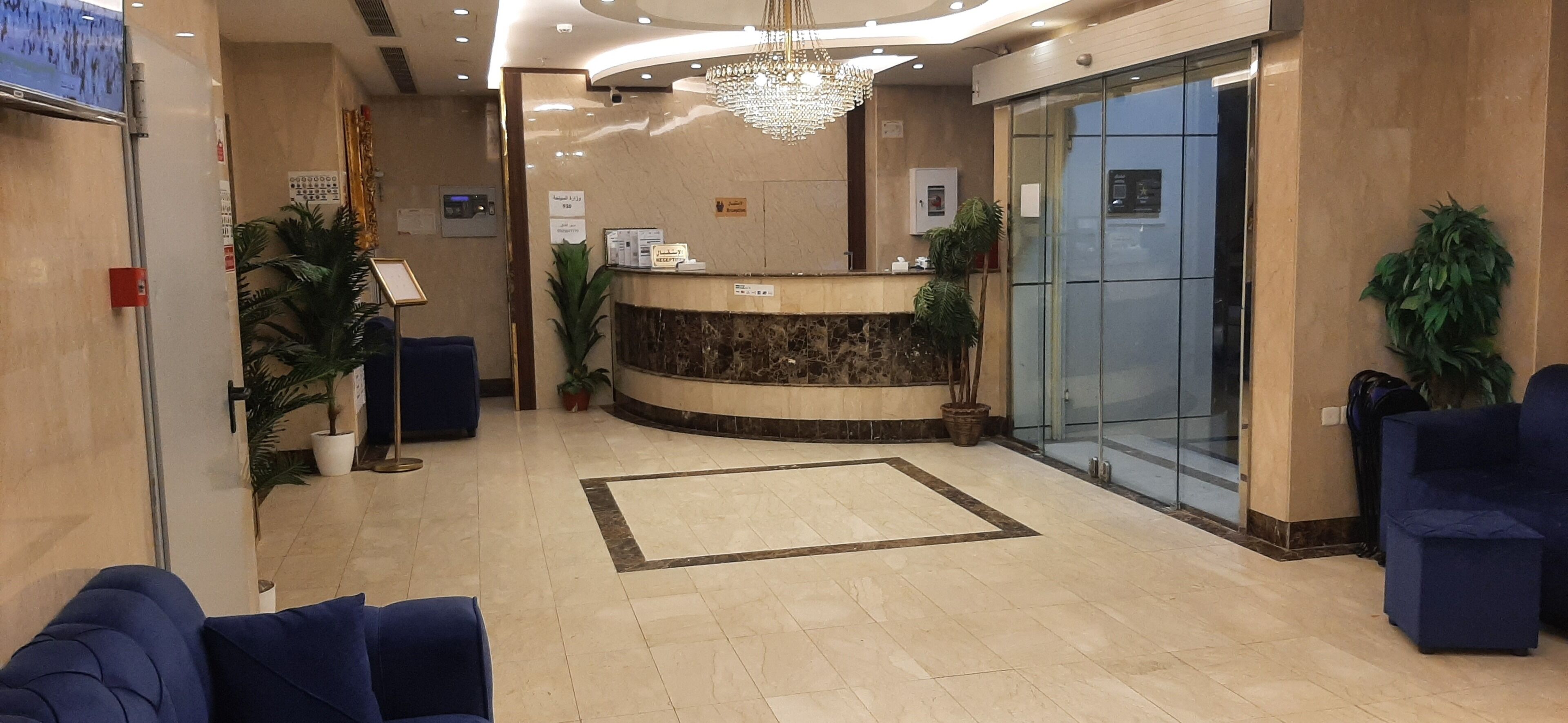 Et hotellets reception med en marmor disk, blåt siddearrangement, en lysekrone og potteplanter.