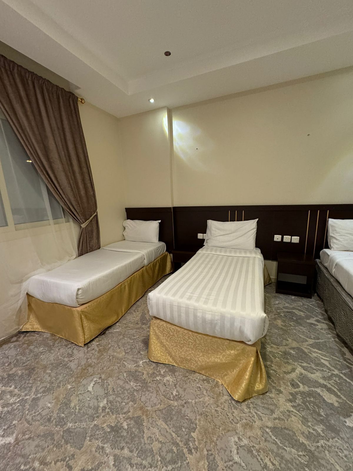 A hotel room with two single beds, a window with curtains, a marble floor, and a wooden headboard.