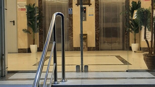 A hotel entrance with a glass door, two elevators, a chandelier, and a staircase with metal railings. - Taj Aldahabia Hotel - Makkah - Al Rawda فندق تاج الذهبية - مكة - الروضة (Makkah)