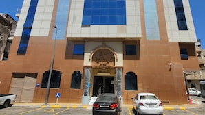 A multi-story hotel with a prominent entrance, a blue-tiled facade, and a parking lot with cars. - Taj Aldahabia Hotel - Makkah - Al Rawda فندق تاج الذهبية - مكة - الروضة (Makkah)
