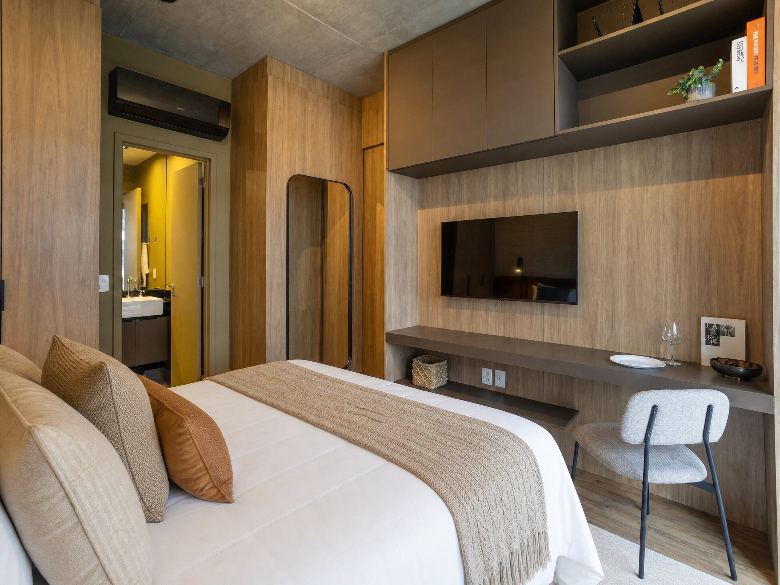 Una habitación de hotel moderna con una cama, un escritorio con una silla, un televisor y un baño visible a través de una puerta abierta.