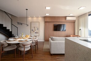 A modern living space with a dining area, a sofa, a flat-screen TV mounted on the wall, and a staircase. - VN Millennium (São Paulo)