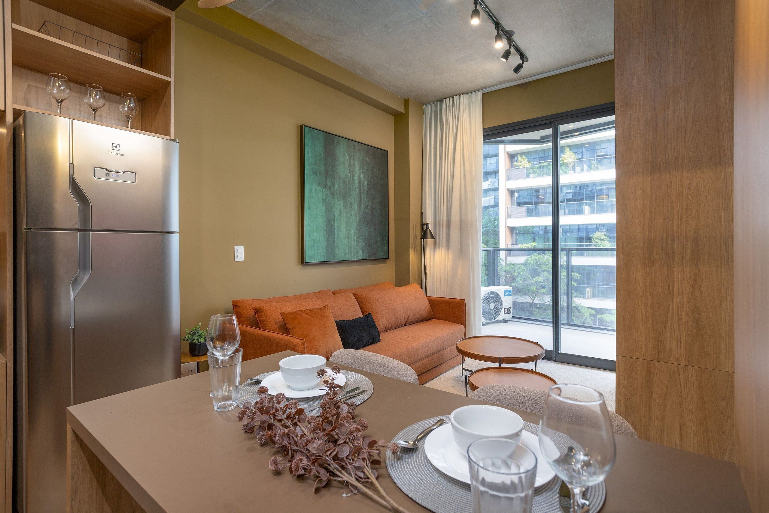 Una cocina moderna con refrigerador integrado, un comedor con una mesa lista para dos personas y un sofá al fondo.
