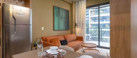 Una cocina moderna con refrigerador integrado, un comedor con una mesa lista para dos personas y un sofá al fondo.