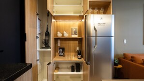 Una cucina compatta con frigorifero integrato, mensole in legno e un piccolo piano di lavoro.
