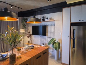 A modern kitchen with a wooden countertop, two pendant lights, a built-in TV, and a stainless steel refrigerator. - VN Millennium (São Paulo)