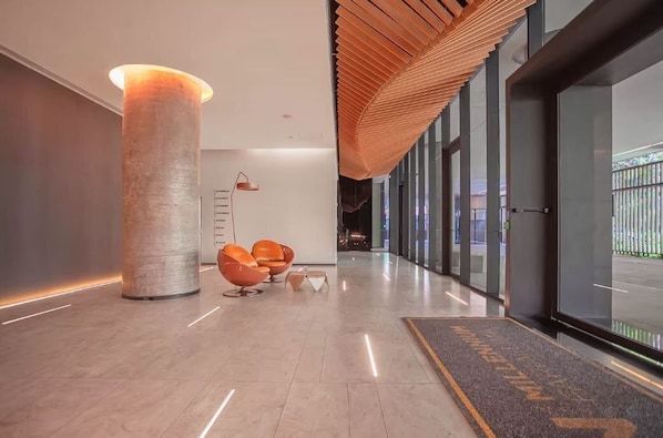 A modern lobby with a large cylindrical column, orange chairs, and a wooden slatted ceiling.