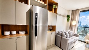 A modern kitchen with a stainless steel refrigerator, built-in cabinets, and a dining area with a grey sofa and a view of the city. - VN Millennium (São Paulo)