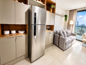 A modern kitchen with a stainless steel refrigerator, built-in cabinets, and a dining area with a grey sofa and a view of the city. - VN Millennium (São Paulo)
