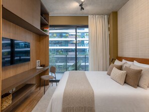 A modern hotel room with a large bed, a flat-screen TV mounted on the wall, a small seating area, and a balcony with a view of the city. - VN Millennium (São Paulo)