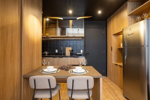 A modern kitchen with wooden cabinets, a stainless steel refrigerator, and a dining area with two chairs and a table set for two. - VN Millennium (São Paulo)