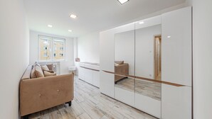 A modern bedroom with a large mirror, a sofa, and a view of the city through the window. - Apartamenty Sun & Snow 1000-lecia Państwa Polskiego (Wladyslawowo)
