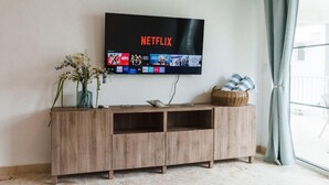 Un salon avec un meuble TV en bois, un téléviseur à écran plat diffusant Netflix et un panier en osier posé sur le meuble.