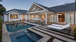 Een modern huis met een zwembad, een overdekt terras en een goed verlicht interieur.