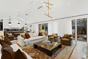 Un vaste salon au design moderne, comprenant une grande table basse, des canapés et un coin repas avec une cuisine en arrière-plan.