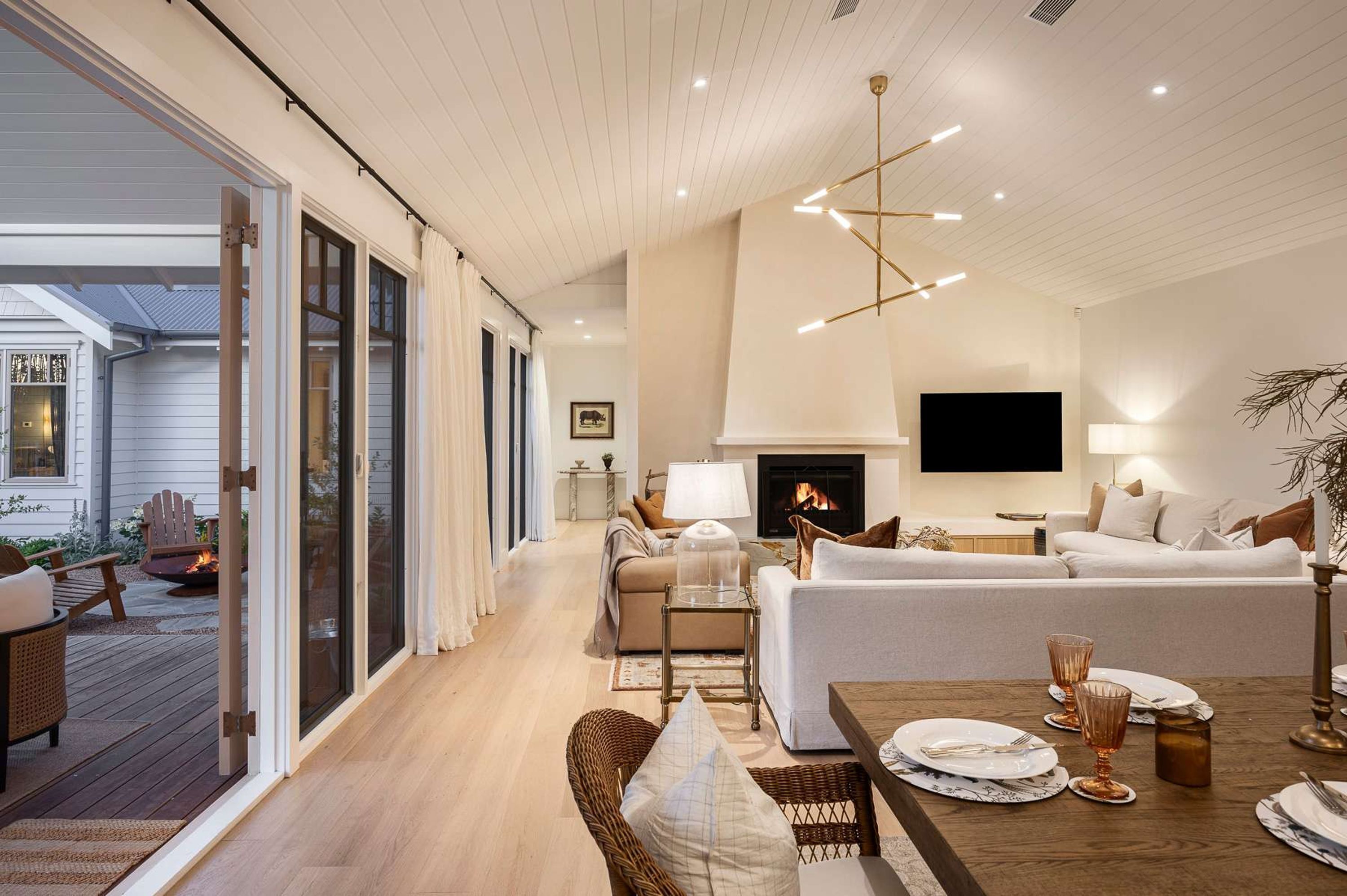 A spacious living room with a fireplace, a dining area with a table set for four, and a large sliding glass door leading to an outdoor deck.