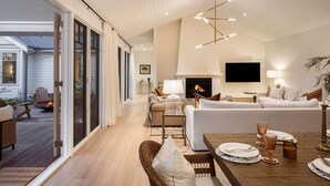 Een ruime woonkamer met een open haard, een eetgedeelte met een tafel gedekt voor vier personen, en een grote schuifpui naar een terras.