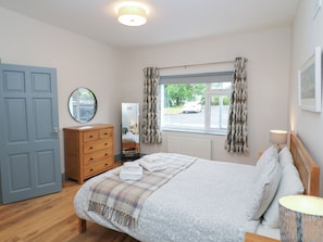A bedroom with a bed, dresser, mirror, window with curtains, and a lamp.