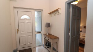 A hallway with a white door, a small table with a lamp, and a wooden bench.