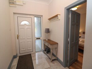 Un pasillo con una puerta blanca, una mesita con una lámpara y un banco de madera.
