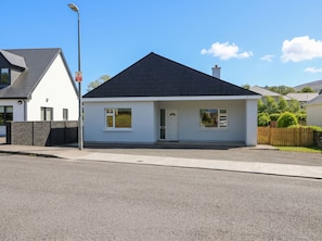 A modern single-story house with a dark roof, white exterior walls, and a small front porch.