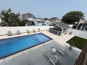 Um quintal com piscina, cadeiras de descanso, área de churrasco e um pequeno deck.