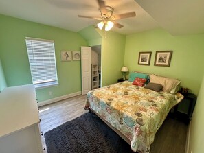 Cozy retreat with a comfortable bed, nightstand, and ceiling fan, plus framed artwork on the wall.