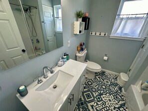 Features a large mirror, a sink with a single faucet, a toilet, and a window with a curtain.