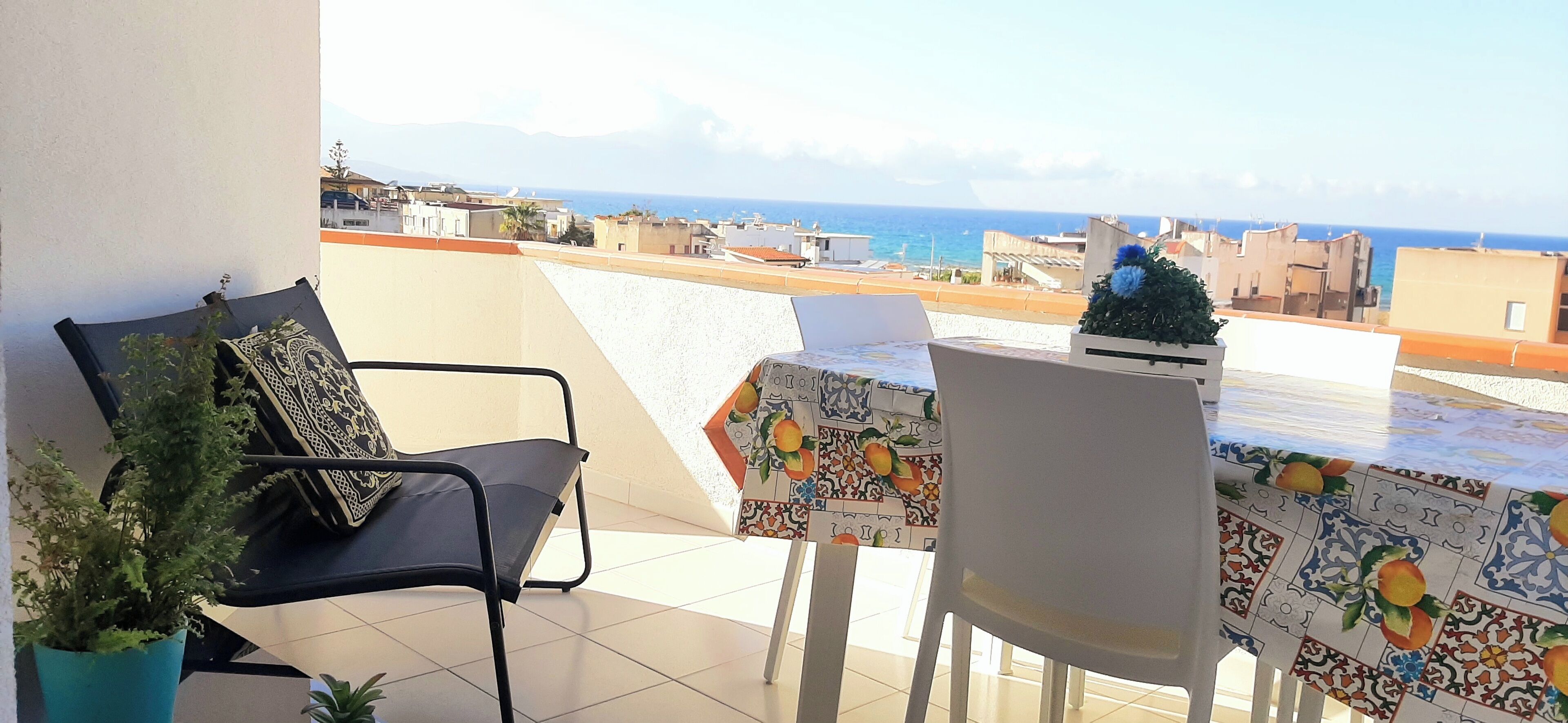 Un balcon avec une table et des chaises, un pot de fleurs et une vue sur la mer et les bâtiments.