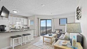 A modern apartment with a kitchen, dining area, and living room. It features a large window, a flat-screen TV, and a cozy seating area.