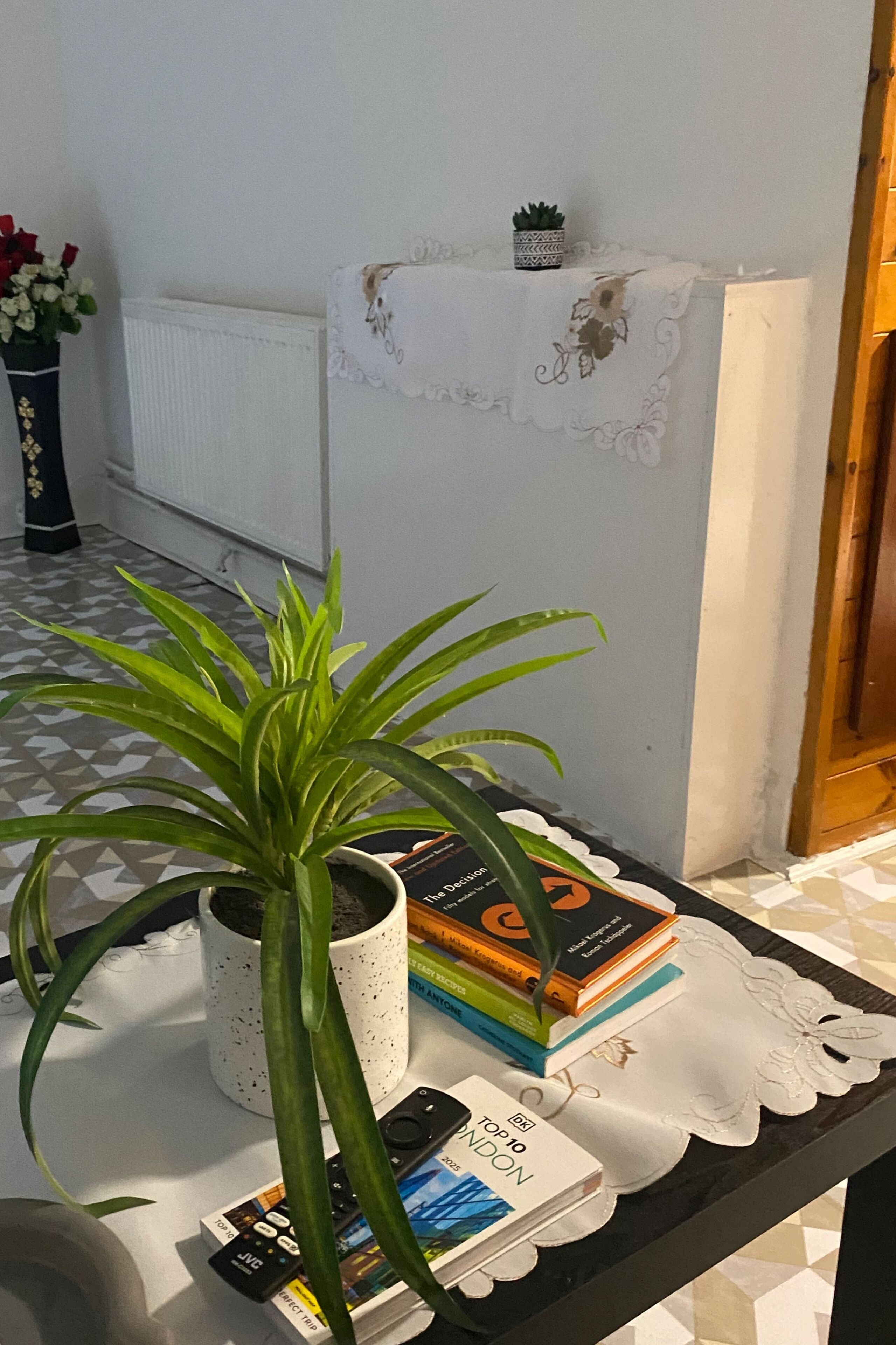A room with a tiled floor, a potted plant, a stack of books, and a white tablecloth on a table.