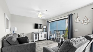 Un salon moderne avec des canapés gris, un téléviseur à écran plat, un ventilateur de plafond et une grande porte-fenêtre coulissante donnant sur un espace extérieur.