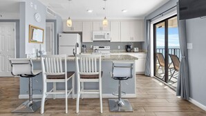 A modern kitchen with white cabinets, a central island with bar stools, a microwave, and a refrigerator. - T1216 at the Myrtle Beach Resort (Myrtle Beach)