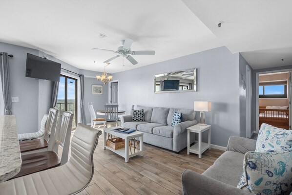 Un salón moderno con un sofá gris, una mesa de centro blanca y un televisor montado en la pared.