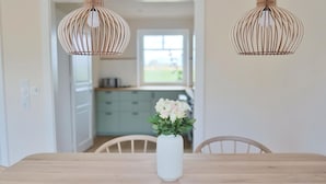 A dining table with a white vase of flowers, two hanging wooden light fixtures, and a view of a kitchen and dining area. - Island idyll Villa Kunterbunt (Fehmarn)